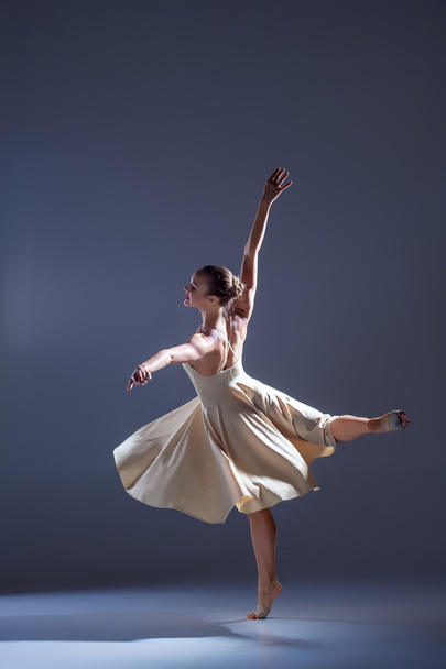 Young beautiful dancer in beige dress dancing on gray background - Fotó, kép