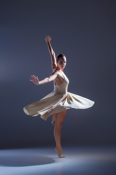 Young beautiful dancer in beige dress dancing on gray background - Foto, Bild
