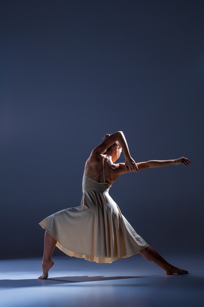 Young beautiful dancer in beige dress dancing on gray background - Foto, Imagen