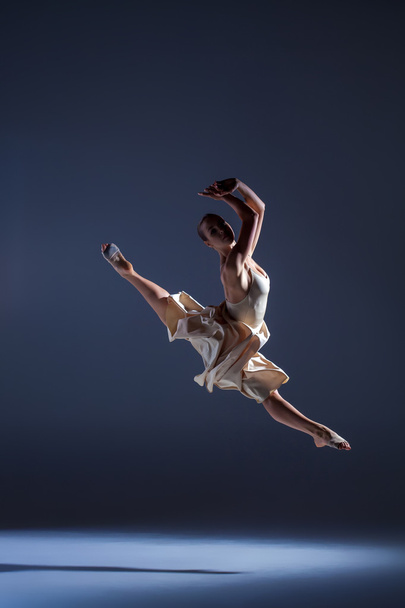 Young beautiful dancer in beige dress jumping on gray background - Fotó, kép