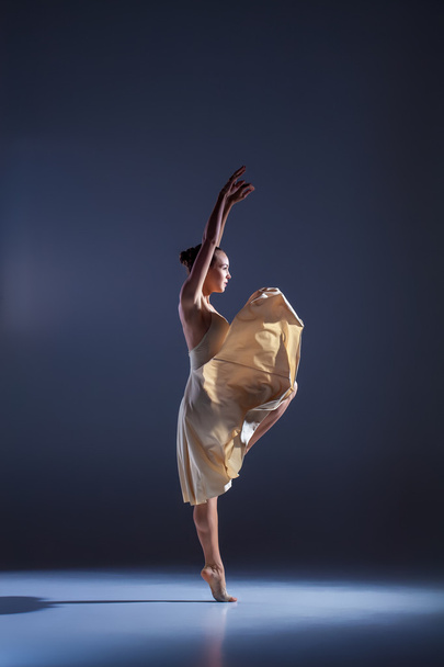 Young beautiful dancer in beige dress dancing on gray background - Photo, Image