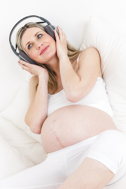 terhes nő az ágyban pihenő fejhallgató - Fotó, kép