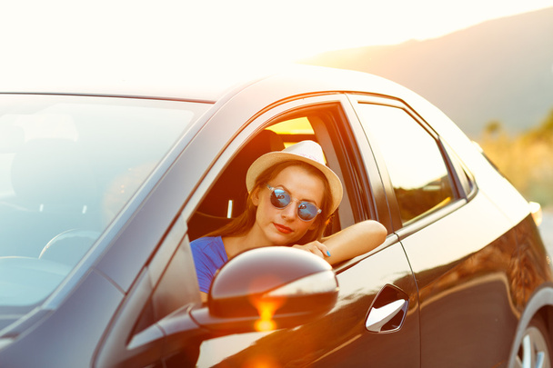 Smiling woman driving a car at sunset - Фото, изображение