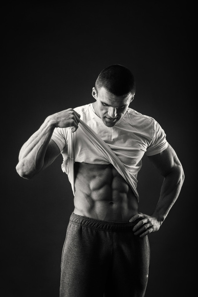Lihaksikas mies urheilutakissa tummalla taustalla
 - Valokuva, kuva