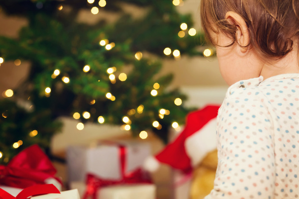 Toddler girl opening gifts in front of the Christmas tree - Φωτογραφία, εικόνα