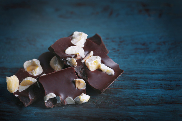 Black chocolate pieces with nuts on color wooden background - Foto, imagen