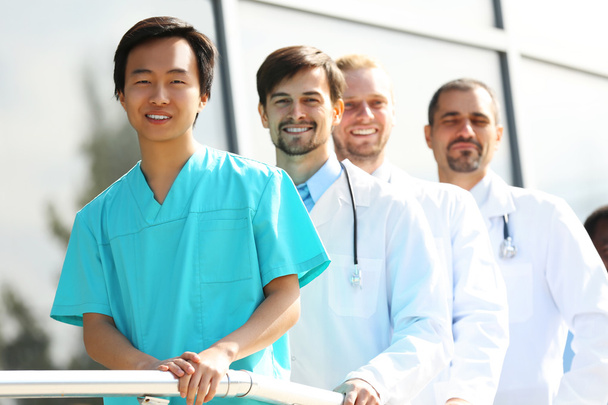 Красиві усміхнені лікарі, що стоять поспіль біля клініки
 - Фото, зображення