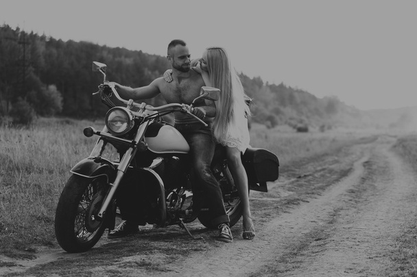 Muscular man with a beautiful woman on a motorcycle middle of a field road - Foto, Bild