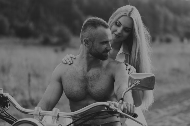 Hombre musculoso con una mujer hermosa en una motocicleta en medio de un camino de campo
 - Foto, Imagen