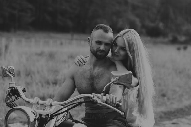 Hombre musculoso con una mujer hermosa en una motocicleta en medio de un camino de campo
 - Foto, imagen