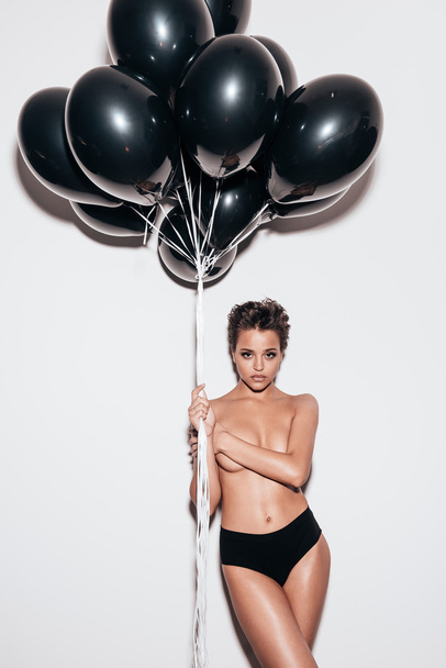 shirtless woman holding black balloons - Фото, изображение