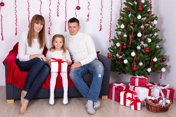 mladá rodina sedí v zařízených obývacího pokoje s vánoční tre - Fotografie, Obrázek