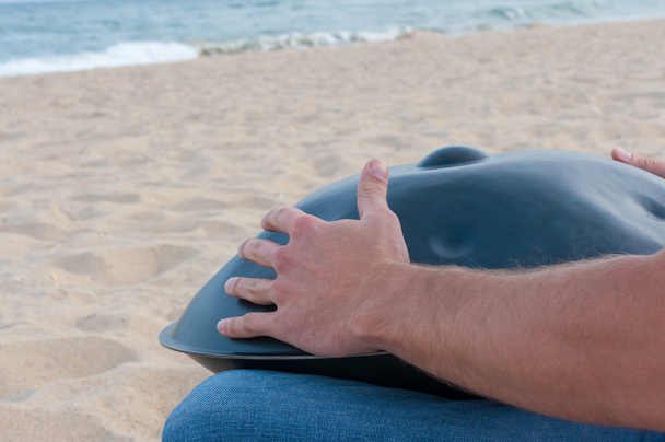 Busker sedersi sulla sabbia e giocare il Hang o handpan con il mare sullo sfondo. L'impiccagione è uno strumento musicale tradizionale etnico tamburo
 - Foto, immagini