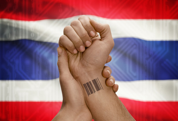 Barcode ID number on wrist of dark skinned person and national flag on background - Thailand - Foto, Imagen