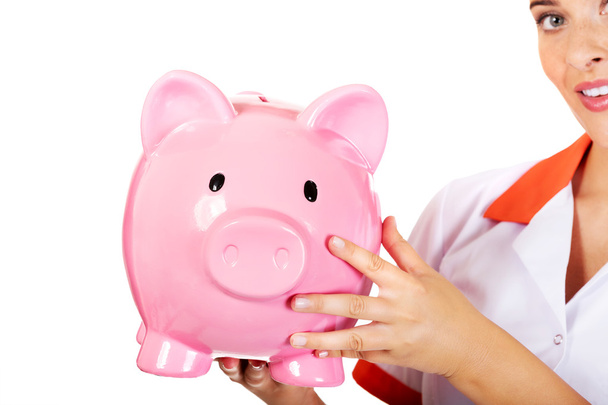 Young beautiful female doctor or nurse holding a piggybank - Foto, afbeelding