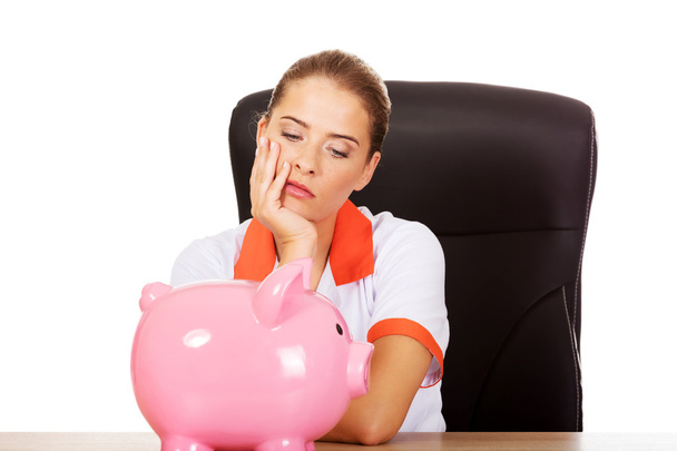 Sad female doctor with piggy bank - Фото, зображення