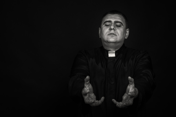 Ammattimainen näyttelijä papin hahmossa tummaa taustaa vasten
 - Valokuva, kuva