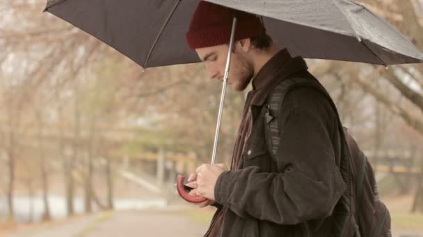 fiatal férfi-egy telefonnal és egy esernyő, az esőben - Felvétel, videó