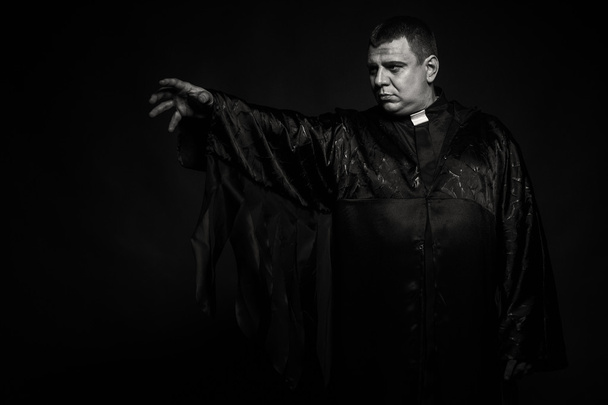 Ammattimainen näyttelijä papin hahmossa tummaa taustaa vasten
 - Valokuva, kuva