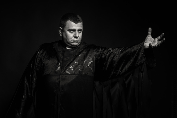 Een professionele acteur in de gedaante van een priester tegen een donkere achtergrond - Foto, afbeelding