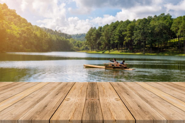 Holzbrett leerer Tisch vor verschwommenem Hintergrund. Perspektive braunes Holz über verschwommenem See im Wald - kann zur Anzeige oder Montage Ihrer Produkte verwendet werden. Frühlingszeit. - Foto, Bild