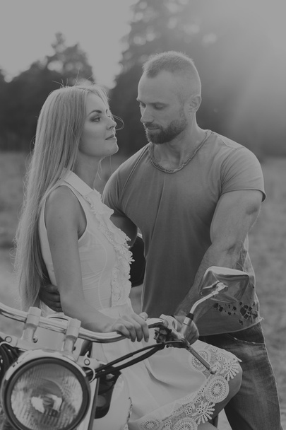 Lihaksikas mies kauniin naisen kanssa moottoripyörällä keskellä kenttätietä
 - Valokuva, kuva