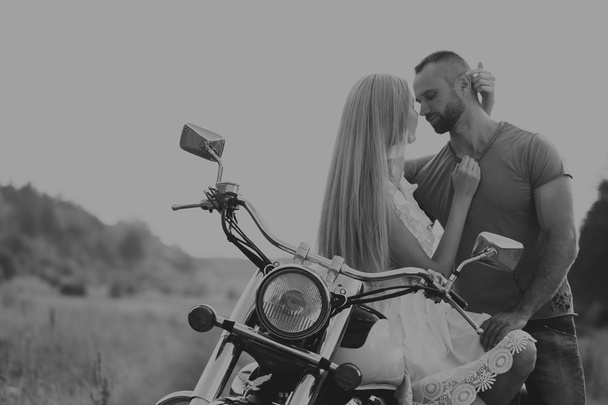 Hombre musculoso con una mujer hermosa en una motocicleta en medio de un camino de campo
 - Foto, Imagen