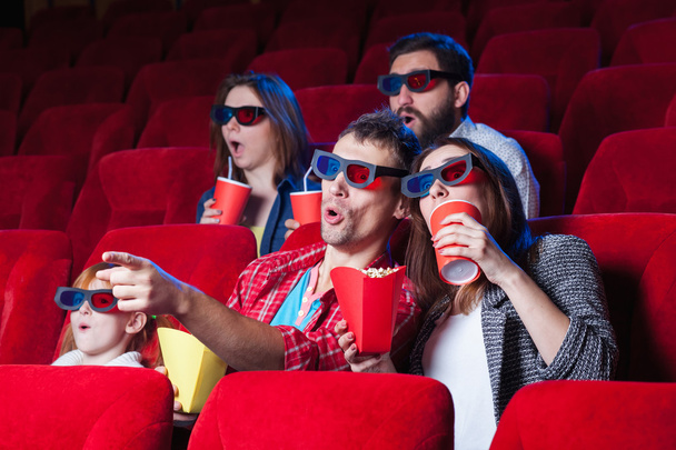 The spectators sitting in the cinema and watching movie  with cups of cola and popcorn. Concept of a variety of human emotions - Foto, afbeelding
