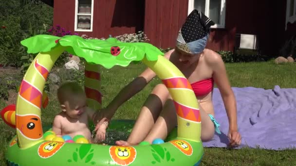 Anne ve bebek şişirilmiş havuzunda yaz aylarında ülkede oynamak. 4k - Video, Çekim