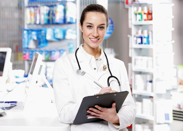 At pharmacy. A smiling young woman pharmacist wearing stethosco - Zdjęcie, obraz