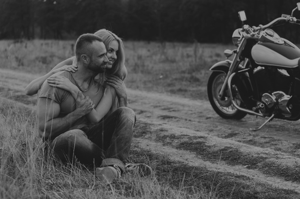 Homem musculoso com uma mulher bonita em uma motocicleta no meio de uma estrada de campo
 - Foto, Imagem