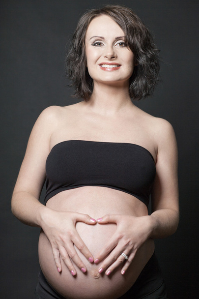 Young pregnant woman posing on black background. - Zdjęcie, obraz