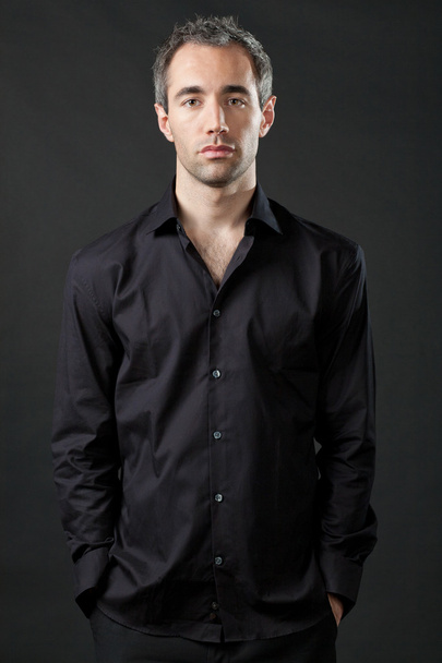 Handsome man posing in black shirt on dark background. - Valokuva, kuva