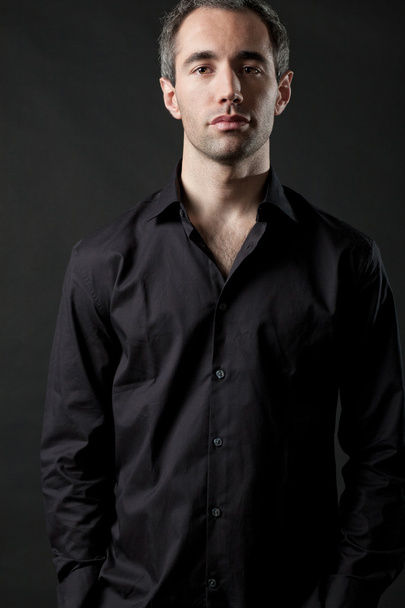 Man posing in black shirt on dark background in studio. - Фото, изображение