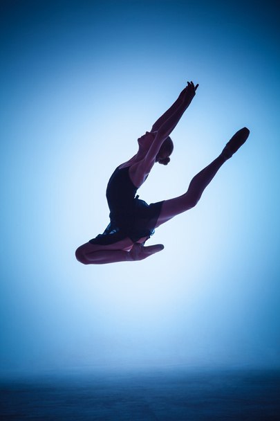The silhouette of young ballet dancer jumping on a blue background. - Foto, Imagen