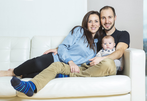 Handsome young father and mother with cute newborn baby on sofa - Zdjęcie, obraz