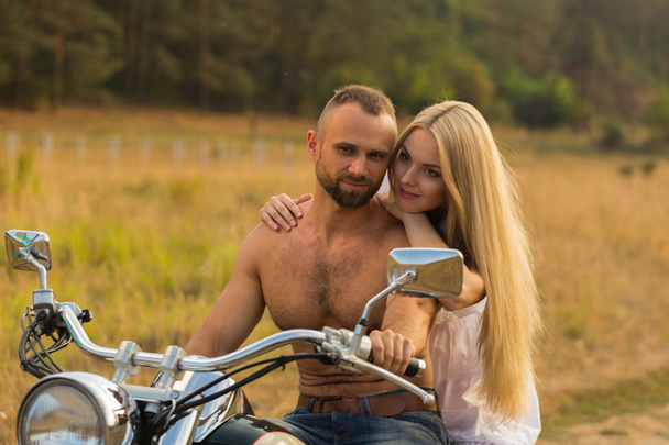 Hombre musculoso con una mujer hermosa en una motocicleta en medio de un camino de campo
 - Foto, imagen