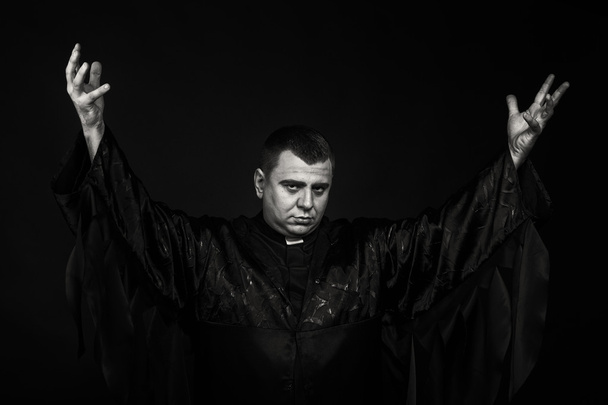 Um ator de palco profissional sob a aparência de um padre contra um fundo escuro
 - Foto, Imagem