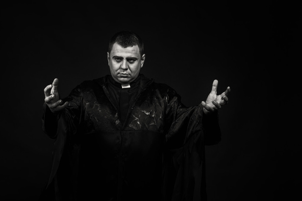 ein professioneller Bühnendarsteller in der Verkleidung eines Priesters vor dunklem Hintergrund - Foto, Bild