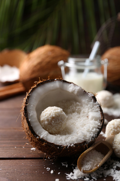 Candies in coconut flakes, glass of milk and fresh coconut on dark wooden background - Photo, image