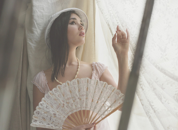 Jonge mooie sexy meisje met donker haar zittend op de vensterbank met de Venetiaanse ventilator - Foto, afbeelding