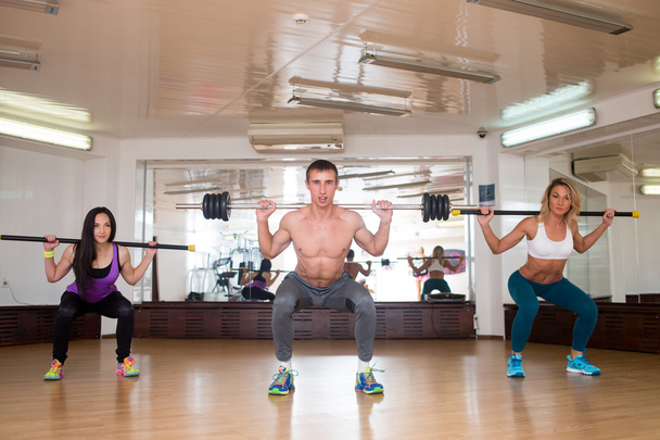 group of smiling people working out with barbells in the gym - Photo, Image