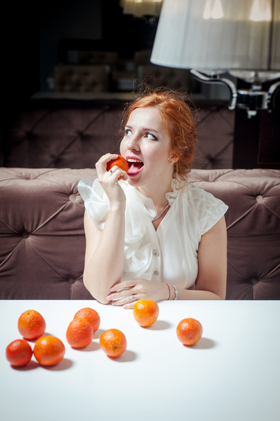 Bella ragazza dai capelli rossi con mandarini in abito bianco
 - Foto, immagini