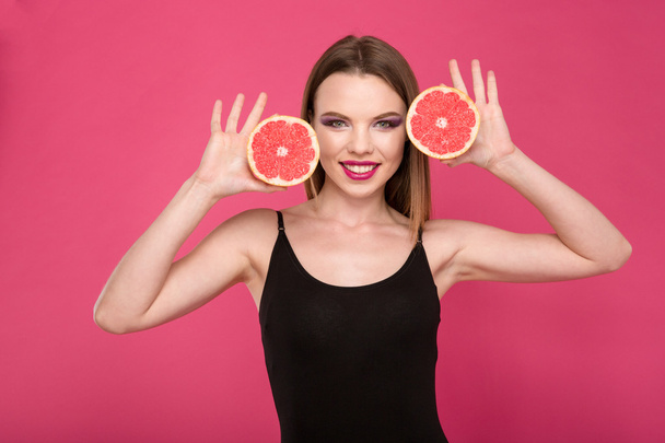 Happy smiling girl posing with two halves of grapefruit - Фото, изображение