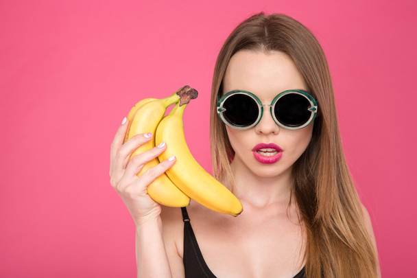 Closeup of young female in glasses holding bananas - Foto, Imagen
