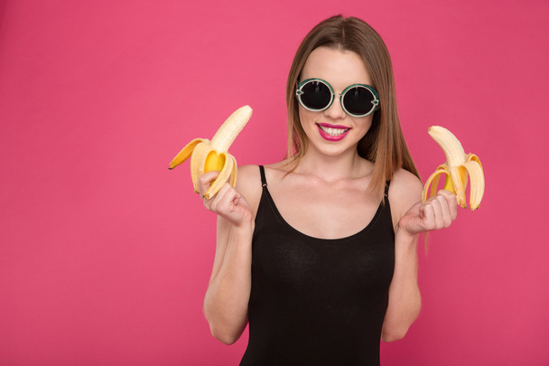 Portrait of positive attractive young woman holding two bananas - Fotografie, Obrázek
