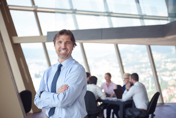 портрет бизнесмена в современном светлом офисе в помещении со своей командой в группе, работающей вместе на заднем плане
 - Фото, изображение
