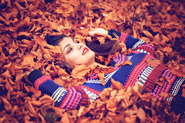 Осенняя женщина лежит над листьями и улыбается, вид сверху
 - Фото, изображение