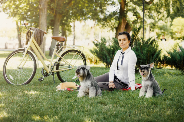 Jonge vrouw met honden en fiets met picknick in het park - Foto, afbeelding