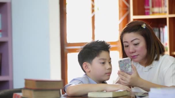 Ευτυχισμένος Ασίας αγόρι και τη μητέρα είναι τραβήξετε μια φωτογραφία από κινητό τηλέφωνο στο βιβλιοθήκη - Πλάνα, βίντεο